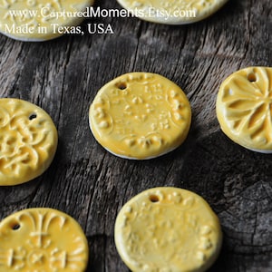 May include: Six yellow ceramic ornaments with different embossed designs. The ornaments are round and have a hole at the top for hanging. They are on a wooden surface.