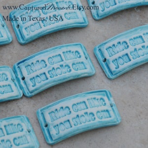 May include: A set of six blue ceramic tiles with the phrase "Ride em like you stoke em" in white lettering. The tiles are slightly curved and have a rustic, handmade look.