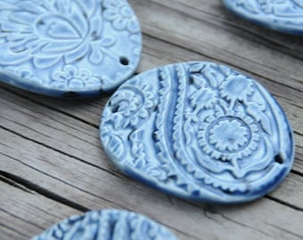 May include: Blue ceramic oval-shaped ornaments with intricate floral and paisley designs. The ornaments have a raised, textured surface and a light blue glaze.
