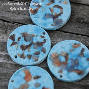 May include: Four round ceramic tiles with a blue glaze and brown, orange, and silver accents. The tiles have a speckled appearance and are perfect for crafting projects.