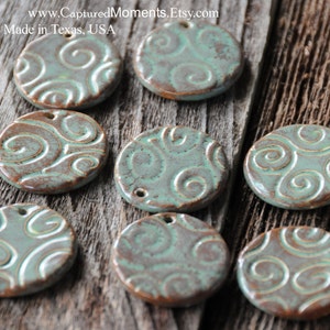May include: Ten round ceramic pendants with a teal glaze and a brown swirl design. The pendants have a hole at the top for hanging.