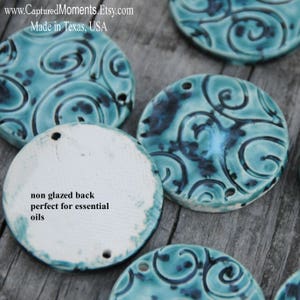 May include: Four teal blue ceramic round discs with a swirl pattern and black accents. The back of the discs are unglazed and white. The text "non glazed back perfect for essential oils" is written on one of the discs.