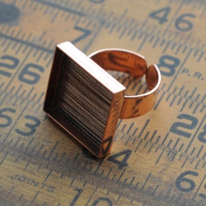 May include: A copper ring with a square bezel, perfect for adding a personal touch to your jewelry. The bezel is designed to hold a small piece of glass or other material.