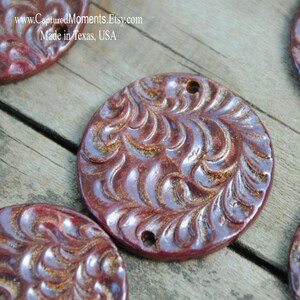 May include: A set of four round, red ceramic ornaments with a raised, swirling pattern. The ornaments have a metallic sheen and two holes for hanging.