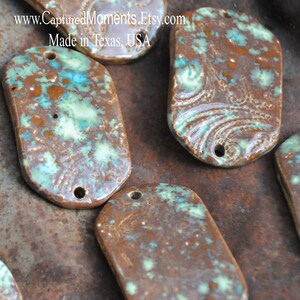 May include: A close-up of several ceramic oval-shaped tags with brown, green, and white glaze. The tags have two holes at the top for hanging. The text "www.CapturedMoments.Etsy.com Made in Texas, USA" is visible in the top left corner of the image.