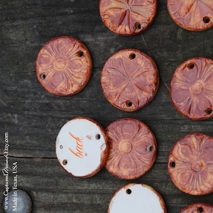 May include: Ten round ceramic tiles featuring a floral design. The tiles are a light brown colour with a darker brown glaze. The reverse of one tile is shown, which is white with the word "back" written on it.