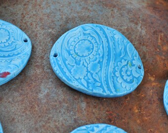 May include: Four blue ceramic tiles with a paisley pattern. The tiles are oval shaped and have a hole in the top for hanging.