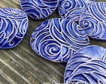 May include: Six blue ceramic ornaments with a swirling, wave-like pattern. The ornaments are glazed with a light blue glaze and have a white outline. The ornaments are arranged in a semi-circle on a wooden surface.