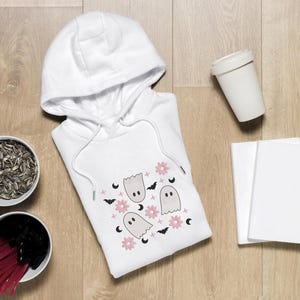May include: White hooded sweatshirt with a print of pink flowers, white ghosts, and black bats.
