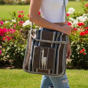 May include: A brown and white striped shoulder bag with a flap and a front pocket featuring a white llama design. The bag is carried by a person wearing a white off-the-shoulder top and blue jeans. The bag has a woven texture.