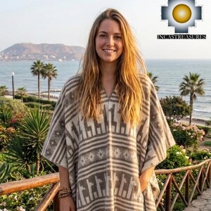 May include: A beige and brown poncho with a geometric pattern and fringe. The poncho is worn over blue jeans and brown boots. The background includes a coastal view with palm trees and a wooden walkway.