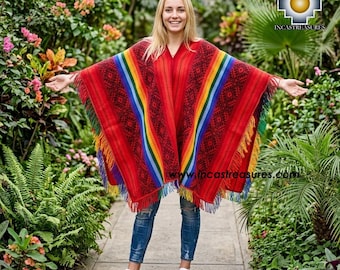 May include: A vibrant red poncho with a rainbow stripe design and fringed edges. The poncho features a geometric pattern and is worn over blue jeans and white sneakers. The image is set outdoors with lush greenery in the background.