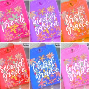May include: A collection of colorful crewneck sweatshirts, each displaying a grade level from Pre-K to Fourth Grade. The shirts are in various colors, including pink, purple, orange, red, and blue, and are adorned with floral designs.