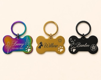 May include: Three bone-shaped pet ID tags with metal rings. The first is iridescent with the name Sunny, a phone number, and tulip engravings. The second is gold with the name Willow and a sun icon. The third is black with the name Bamboo and floral art.