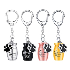 Puede incluir: Cuatro llaveros con un dije de huella de pata y un pequeño colgante de urna en plata, negro, oro rosa y oro. Cada urna tiene el texto "No longer by my side, But Forever in my Heart."