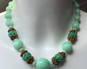 Pode incluir: Um colar de contas verdes e marrons com detalhes florais esculpidos. O colar é feito de contas de jade e plástico marrom.