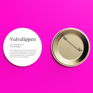 Könnte beinhalten: Ein runder Ansteckbutton mit weißer Vorderseite und schwarzem Text, der den Begriff Vulvalippen definiert, inklusive phonetischer Aussprache und einem beschreibenden Absatz auf Niederländisch. Die Rückseite ist metallisch silber mit Nadel.