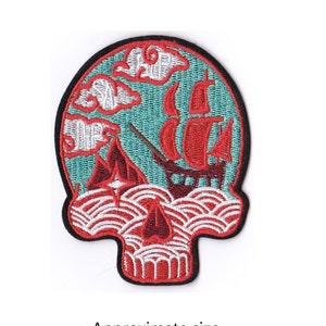 May include: Red and white embroidered skull patch with a blue and red sailboat and clouds inside. The patch is approximately 3.5 inches by 2.75 inches.
