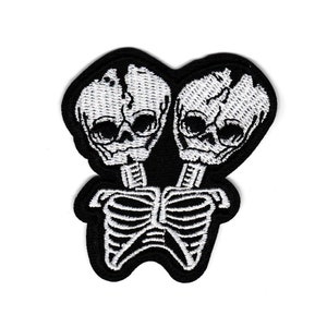 May include: Black and white embroidered iron-on patch featuring two connected skeletons with skulls. The patch is approximately 2.75 inches by 2.5 inches.