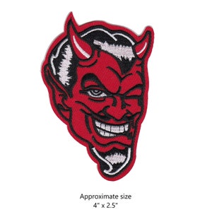 May include: Embroidered patch featuring a red devil face with a winking eye and a wide grin. The devil has black hair and horns, with white accents. Approximate size is 4 inches by 2.5 inches.