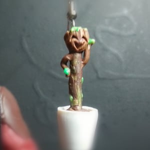 May include: A small, brown, potted plant with green leaves and a smiling face. The plant is in a white pot and is hanging from a string.
