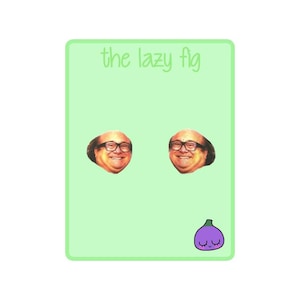 May include: A pair of earrings featuring a cartoon image of the character Frank Reynolds from the television show It's Always Sunny in Philadelphia. The earrings are on a green background with the text "the lazy fig" at the top. A cartoon purple fig with a smiling face is at the bottom of the image.