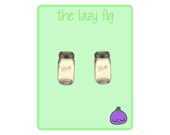 May include: Two clear glass mason jars with the word "Ball" printed on the side. The jars are on a green background with the text "the lazy fig" at the top and a cartoon purple fig at the bottom.
