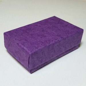 May include: A small, purple gift box with a textured paper finish. The box is ideal for holding small items like jewelry or other trinkets.