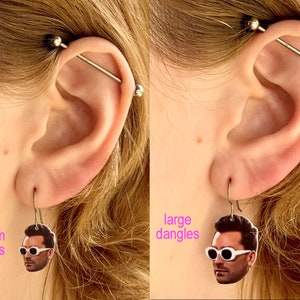 May include: Two pairs of earrings with a person's face on them. The earrings on the left are labeled "medium dangles" and the earrings on the right are labeled "large dangles".