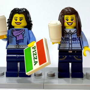 May include: Two Lego minifigures, one with a blue sweater and a purple scarf, the other with a blue sweater with a white snowflake pattern, both holding a white coffee cup. The minifigure on the left is holding a green, white, and red box that says "PIZZA" on it.