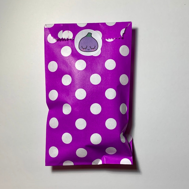 May include: A purple gift bag with white polka dots and a sticker of a cartoon fig with a smiling face.