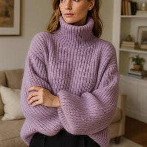 May include: A lilac ribbed turtleneck sweater with long, voluminous sleeves. The model is wearing black trousers. The background shows a neutral-toned room with a sofa and bookshelves.