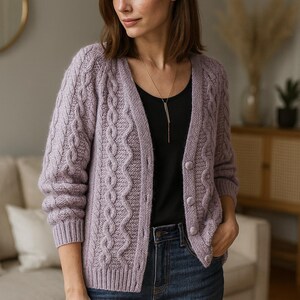 Puede incluir: Un cárdigan de punto trenzado de color lila claro con cuello en V y cierre de botones. El suéter tiene un diseño texturizado y se usa sobre una camiseta negra y vaqueros azules. Se ve un collar plateado.