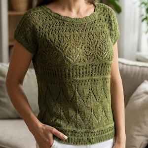 Peut inclure: Un haut en tricot vert olive à manches courtes avec un motif ajouré détaillé. Le haut présente une encolure ronde et un ourlet côtelé. La femme porte un pantalon blanc. L'arrière-plan comprend un canapé, des plantes et une bibliothèque.