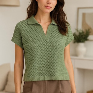 May include: A green short-sleeved polo shirt with a textured knit pattern. The shirt has a V-neck collar and is paired with brown trousers. The overall style is casual and comfortable, suitable for everyday wear.