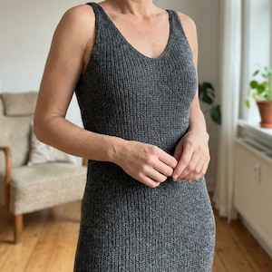 Può includere: Un abito grigio a maglia con scollo a V e stile canotta. L'abito è realizzato in tessuto a maglia a coste e ha una silhouette aderente. L'abito è di colore grigio unito e sembra essere un capo comodo e casual.