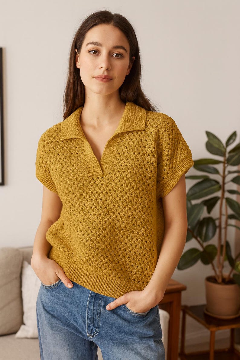 May include: Mustard yellow short-sleeved knit polo shirt with a collared neckline. The shirt has a textured, open-weave design and is paired with blue denim jeans. The model is standing indoors with hands in pockets.