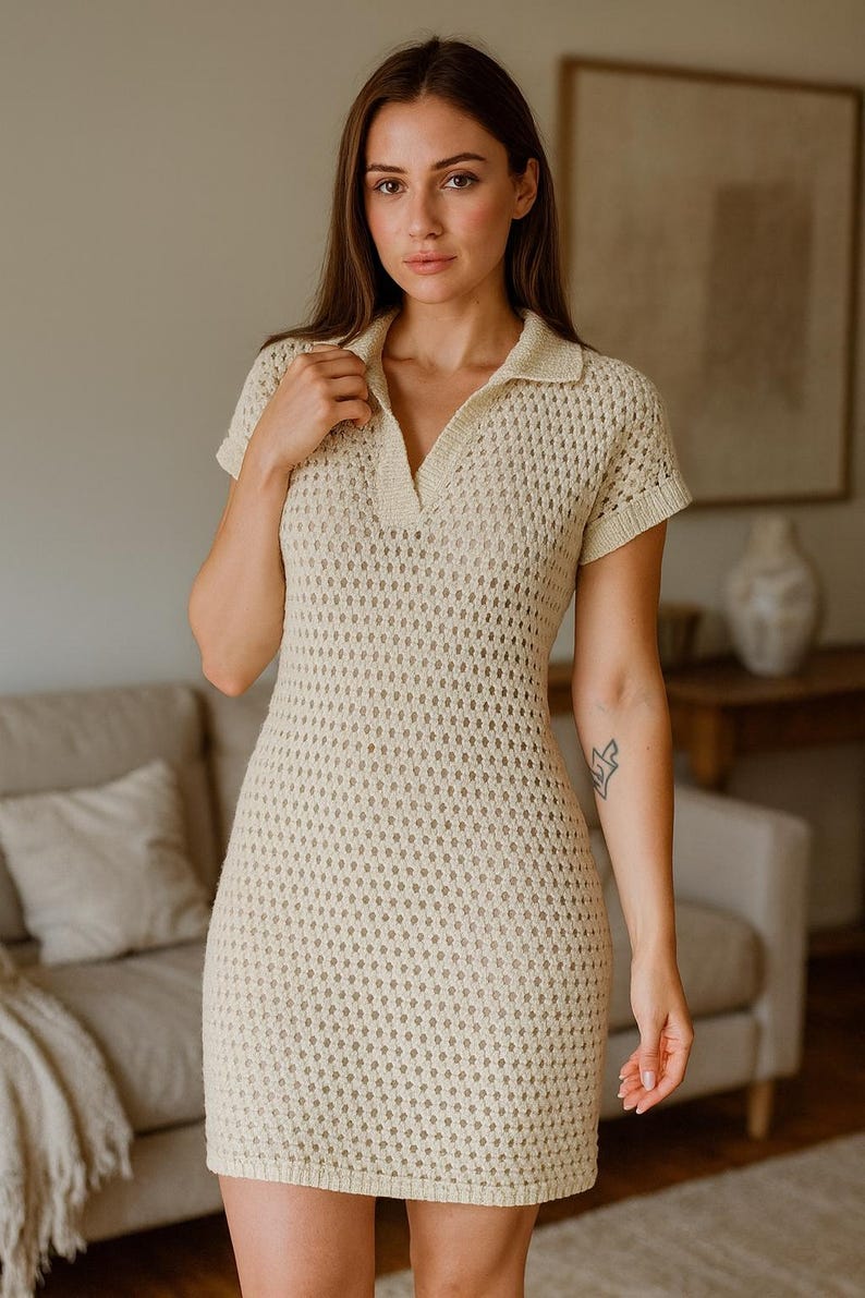 May include: A cream-colored, short-sleeved crochet dress with a collared neckline. The dress has a fitted silhouette and a textured, open-weave design. The model is standing in front of a neutral-toned background.