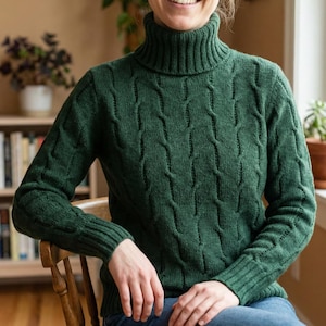 May include: A dark green turtleneck sweater with a cable knit design. The sweater has long sleeves and a ribbed collar and cuffs. The person is sitting in a wooden chair.