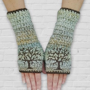 May include: A pair of crocheted fingerless gloves with a brown trim and a tree design in brown yarn on a light blue and green background.