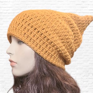 May include: A mustard yellow crocheted beanie with a pointed top. The beanie is made with a simple stitch pattern and has a slouchy fit.