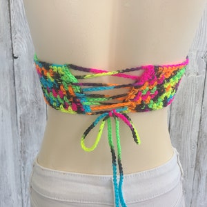 May include: A colorful crochet top with a tie-up back. The top is made with neon pink, green, blue, orange, and black yarn.