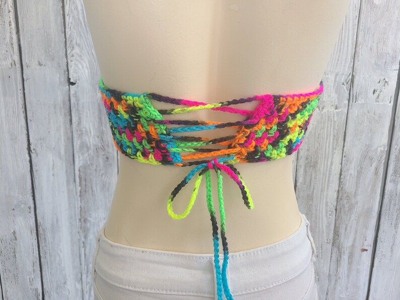 May include: A colorful crochet top with a tie-up back. The top is made with neon pink, green, blue, orange, and black yarn.