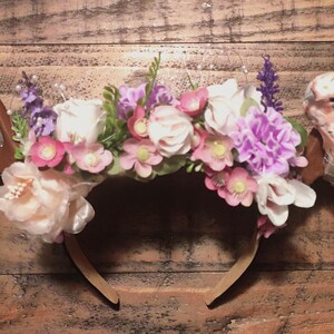 May include: A floral headband with antlers and a delicate tulle veil. The headband is adorned with pink, white, and purple flowers.