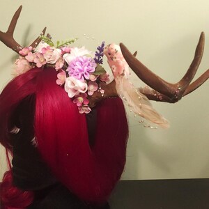 May include: A brown antler headband with pink, white, and purple flowers and a pink bird decoration.