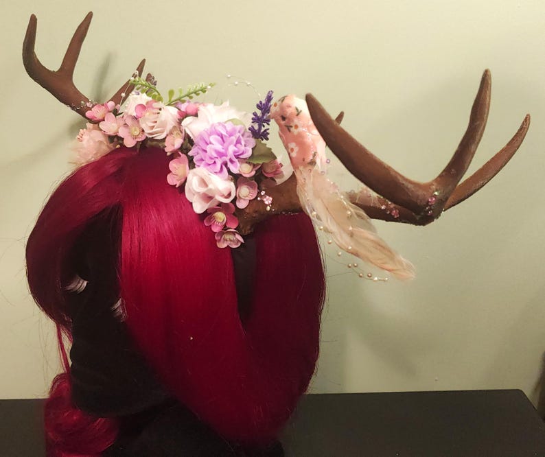 May include: A brown antler headband with pink, white, and purple flowers and a pink bird decoration.