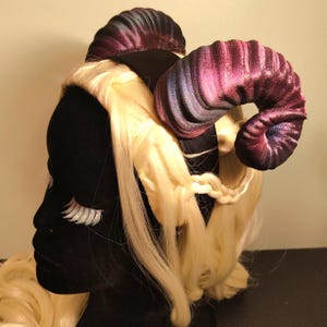 May include: A pair of purple and blue velvet horns with a black headband. The horns are curled and have a galaxy-like pattern.