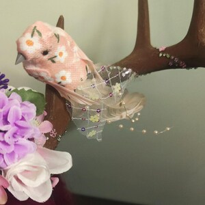 May include: A pair of brown antlers decorated with pink and white flowers, a pink bird with a floral pattern, and a sheer pink and white fabric with sequins.