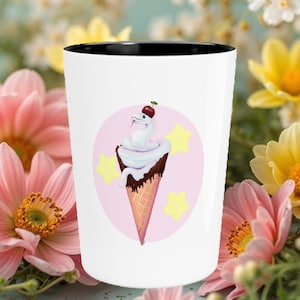 May include: White ceramic mug with a black rim. The mug features a pink background with white stars and a white snake wrapped around a chocolate-covered ice cream cone with a red cherry on top.