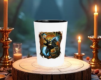 May include: A white ceramic shot glass with a black rim. The glass features a colorful illustration of a figure riding a black horse through a forest. The figure is holding a glowing orb in their hand.
